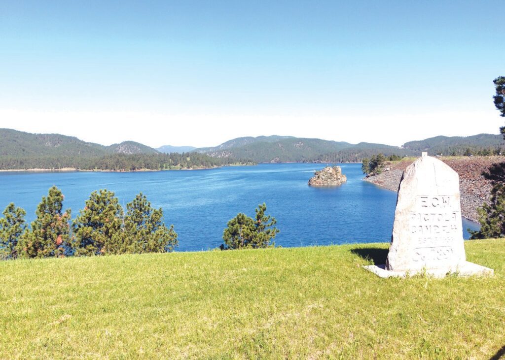 View of Pactola Lake from the Visitors Center. In the foreground, a marker dated 5/18/33 for the long-defunct Pactola Camp F-4, a Civilian Conservation Corps federal relief program. (Photo by Marnie Cook)