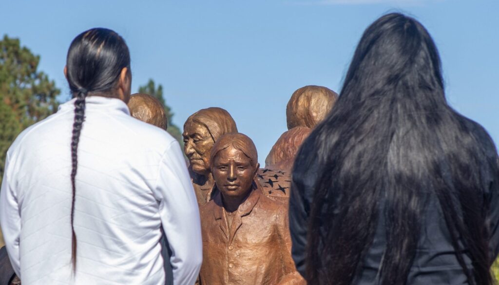 Two Lakota men stand facing the 'Tiwahe' a statue depicting a Lakota family surrounding a young boy who was taken to boarding school. (Photos by Amelia Schafer)