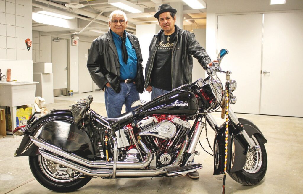 Rev. Dr. Gerald Yellowhawk standing next to son Jim and Jim’s 2000 Indian Motorcycle that is painted and has beadwork done on it for the exhibit. (Photo by Richie Richards)