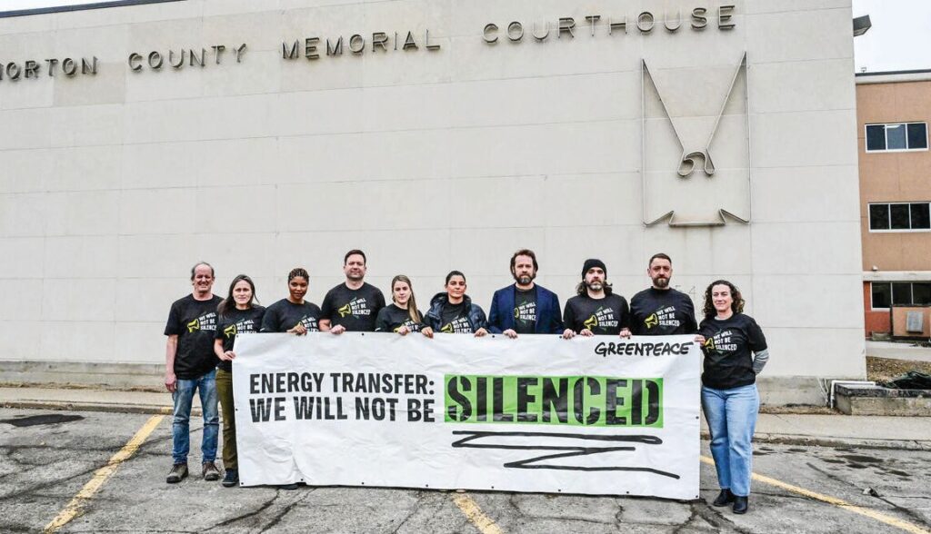 Some of the Greenpeace team hold up a banner outside the Morton County Memorial Courthouse in Mandan, North Dakota March 16, 2025. © Stephanie Keith / Greenpeace