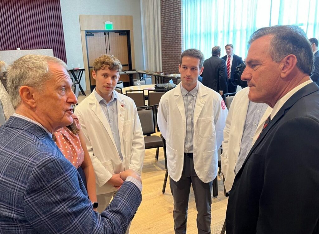 From left, Tim Ridgway, vice president of health affairs and Sanford School of Medicine dean, speaks with medical students including Tanner Smith and Tanner Berg, as well as South Dakota Gov. Larry Rhoden, at the Canopy by Hilton in downtown Sioux Falls on Aug. 14, 2025. (Photo by Makenzie Huber/South Dakota Searchlight)